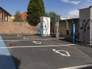 A parking area with electric vehicle charging stations, marked parking spaces, and a brick wall in the background. - ibis Lille Lomme Centre (Lille)
