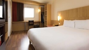 Ein Hotelzimmer mit einem großen Bett, einem Schreibtisch mit Stuhl, einem Kleiderschrank und einem Fenster mit Vorhängen.