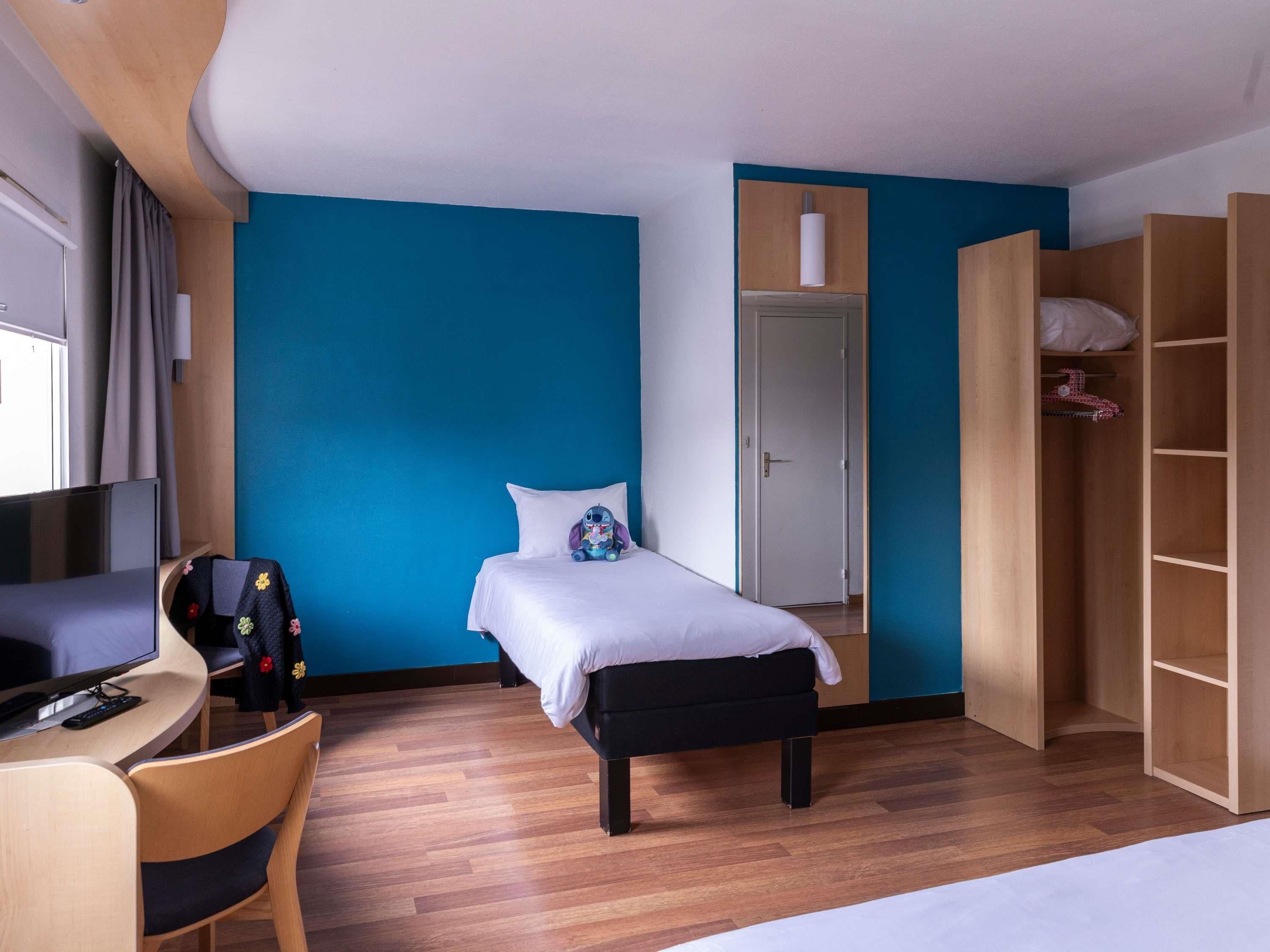 Una habitación con cama, escritorio, silla, armario y televisor.