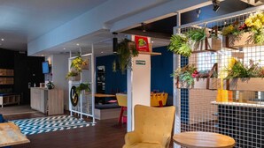 Un intérieur moderne avec un comptoir d’accueil en bois, une chaise jaune, une table ronde et un mur bleu orné d’un motif géométrique.