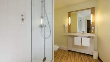A modern bathroom with a glass-enclosed shower, a wooden floor, a white sink with a mirror, and a toilet.