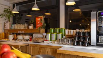 A breakfast bar with a coffee machine, various food items, and a sign indicating a desire for coffee.