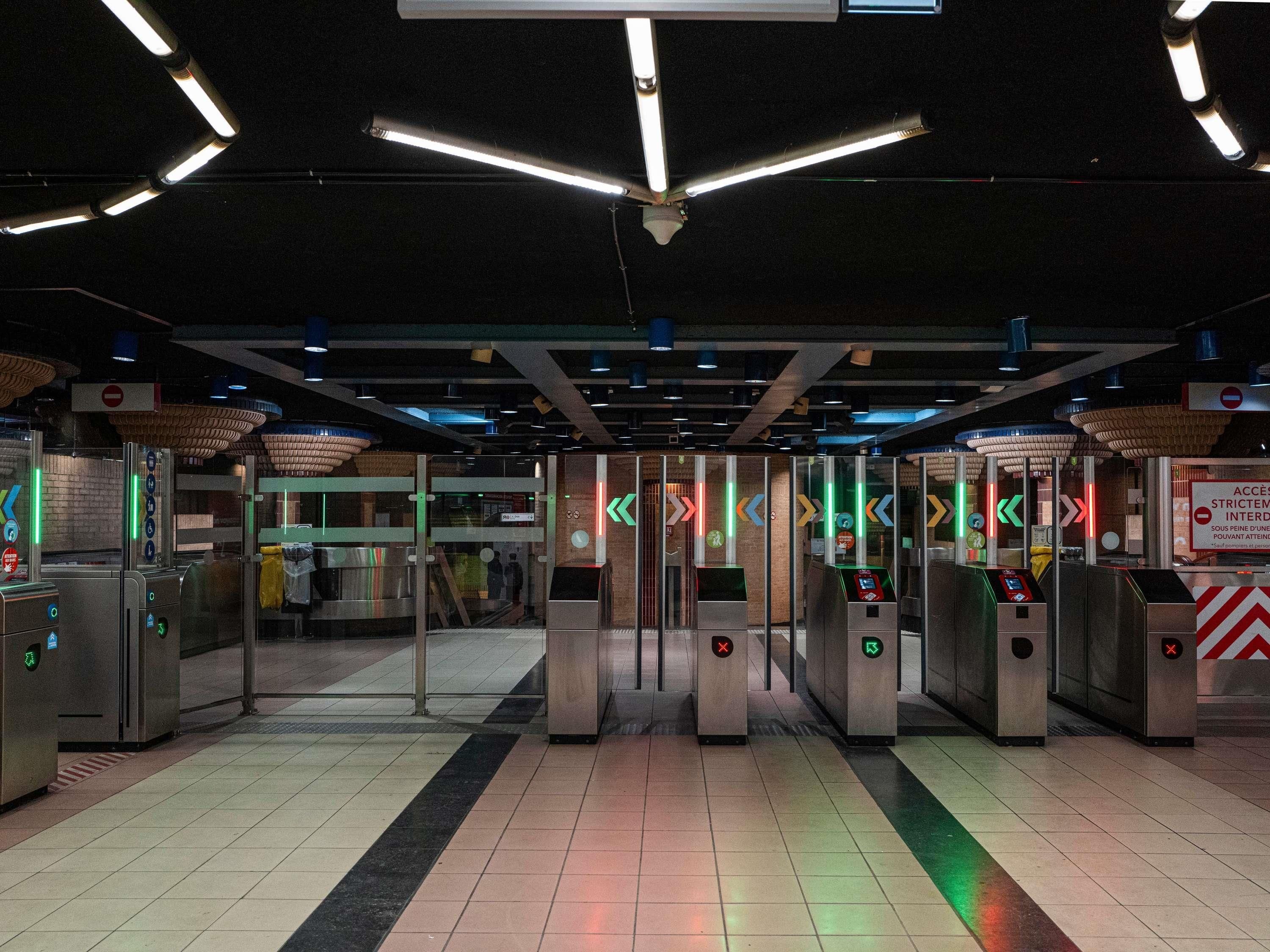 Une station de métro dotée de plusieurs tourniquets, d’un sol carrelé et d’un éclairage au plafond.