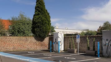 Un área de estacionamiento con estaciones de carga para vehículos eléctricos, un muro de ladrillo y un gran árbol.