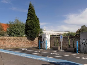 A parking area with electric vehicle charging stations, a brick wall, and a large tree.