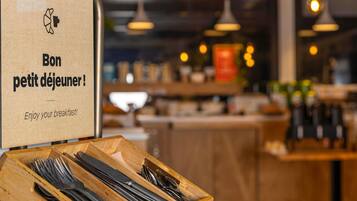 A breakfast setup with a wooden tray of cutlery and a paper bag with a message.
