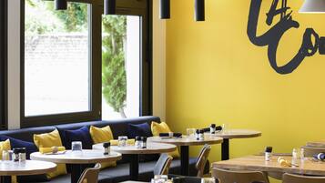 A restaurant interior with round tables, yellow cushions, and a wall with a large black letter design.