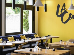 Un interior de restaurante con mesas redondas, cojines amarillos y una pared con un diseño grande de letras negras.