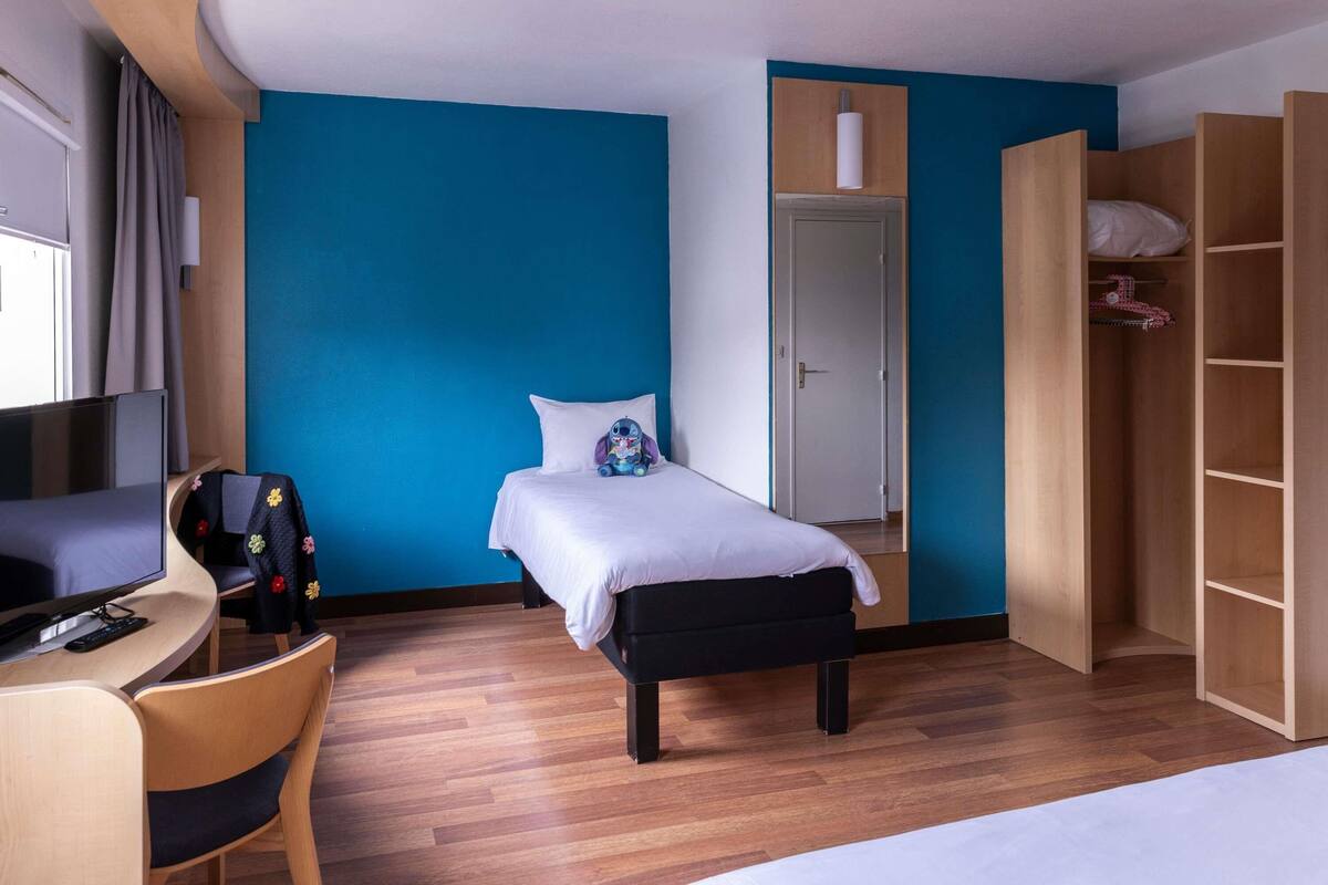 Una habitación con cama, escritorio, silla, armario y televisor.