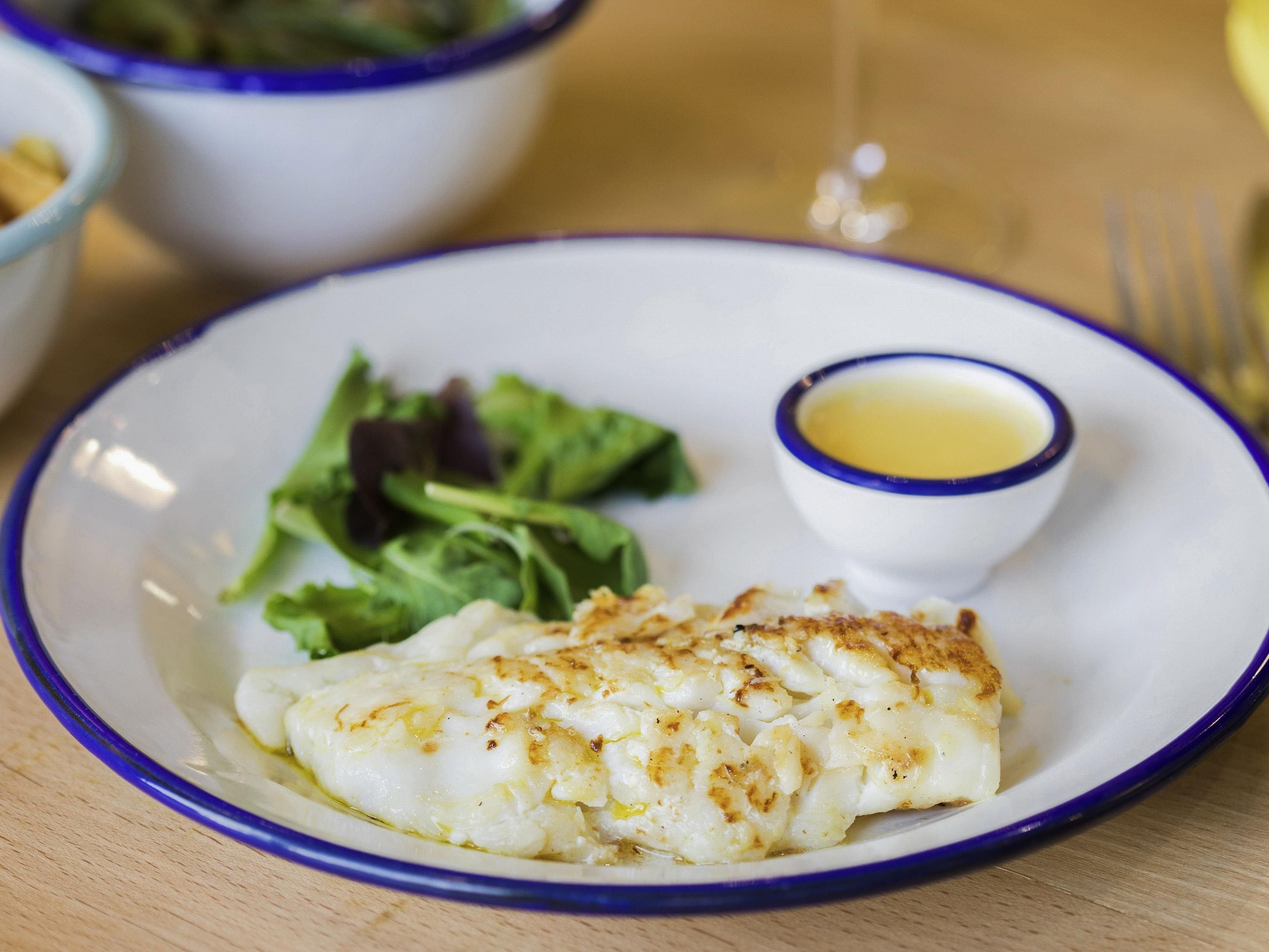 Une assiette avec un morceau de poisson, un petit bol de sauce et une salade en accompagnement.