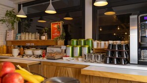 Ein Frühstücksbuffet mit einer Kaffeemaschine, verschiedenen Speisen und einem Schild, das den Wunsch nach Kaffee ausdrückt.