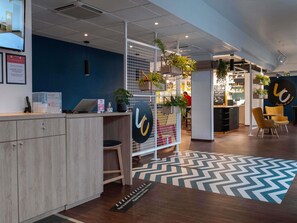 A reception area with a wooden desk, a blue wall, and a chevron-patterned rug. - ibis Lille Lomme Centre (Lille)