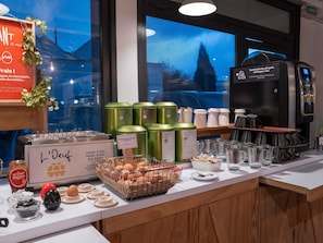 A breakfast buffet with various food items, a coffee machine, and a view of the outside.
