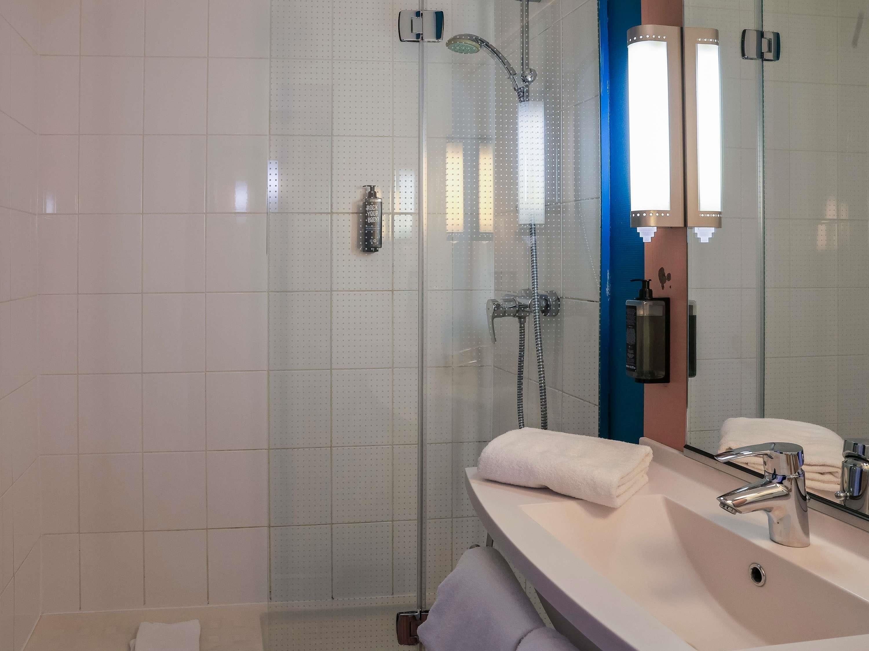 Une salle de bain moderne avec une douche à parois de verre, un lavabo blanc avec un miroir et un porte-serviettes.