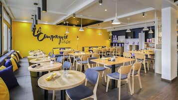 A modern restaurant interior with round tables, blue chairs, and a yellow accent wall.