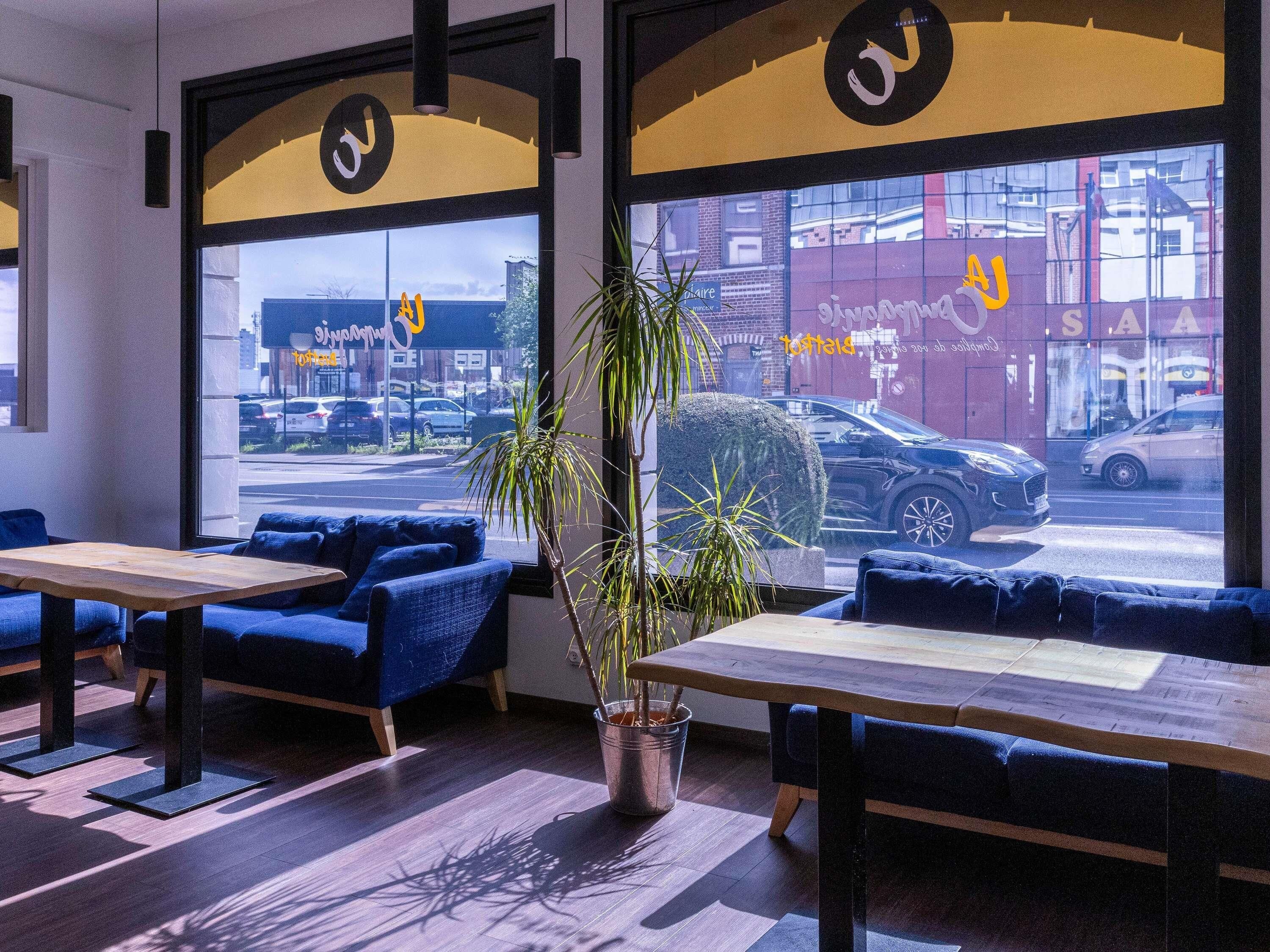 A modern interior with seating, a plant, and a view of the street through large windows.