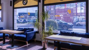 A modern interior with seating, a plant, and a view of the street through large windows.