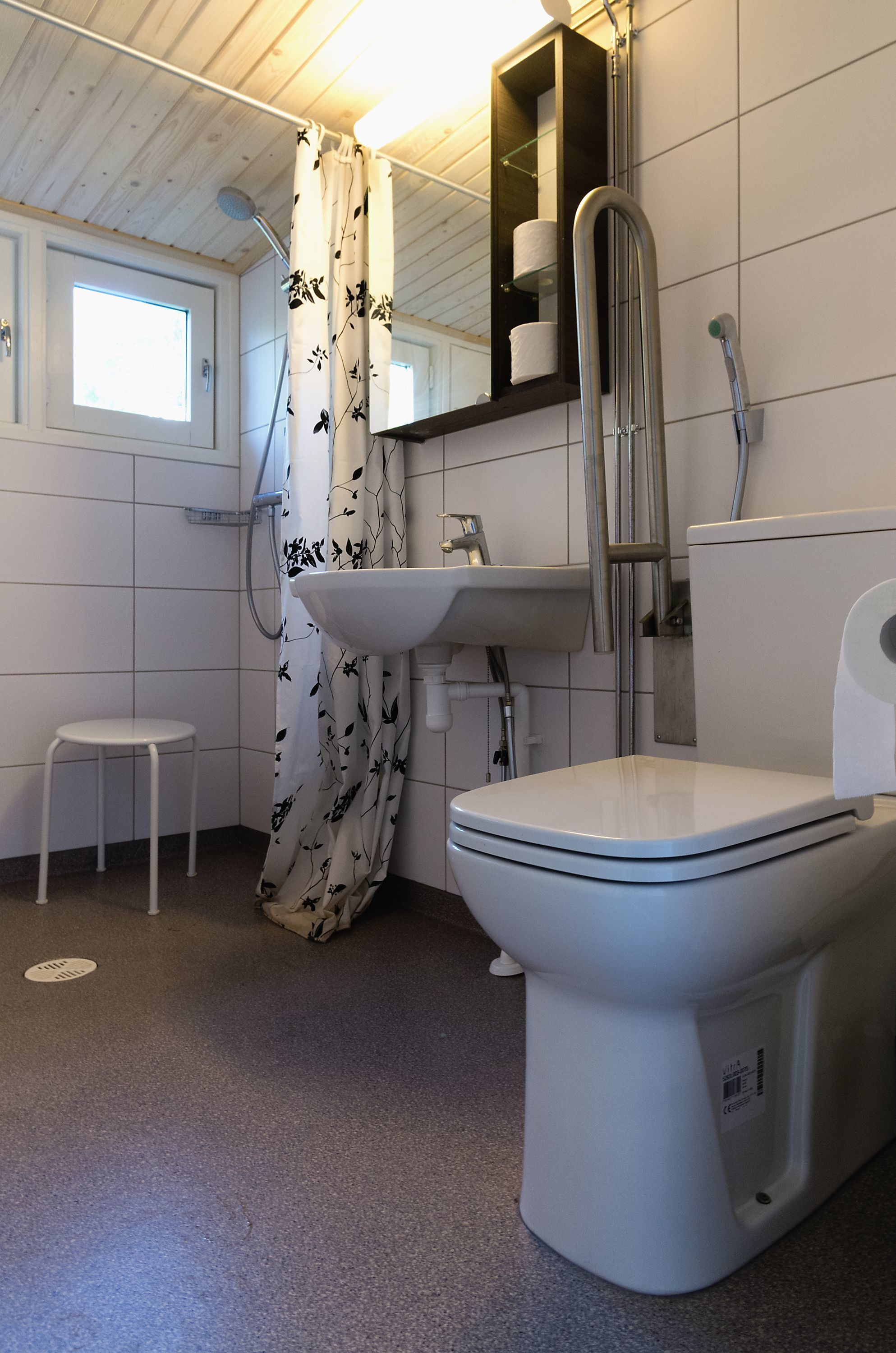 Un baño con inodoro, lavamanos, ducha y un taburete pequeño.