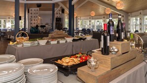 A buffet setup with various food items, wine bottles, and a grill station in a spacious indoor area with natural lighting. - Käringsund Resort & Conference (Eckero)