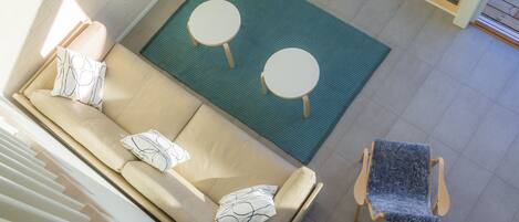 Una sala de estar moderna con un sofá beige, dos mesas redondas y un sillón azul.