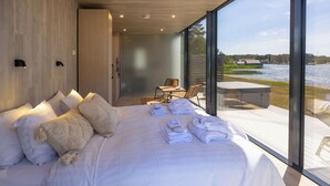 A modern bedroom with a large bed, a seating area with a table and chairs, and a view of a lake through large windows. - Käringsund Resort & Conference (Eckero)