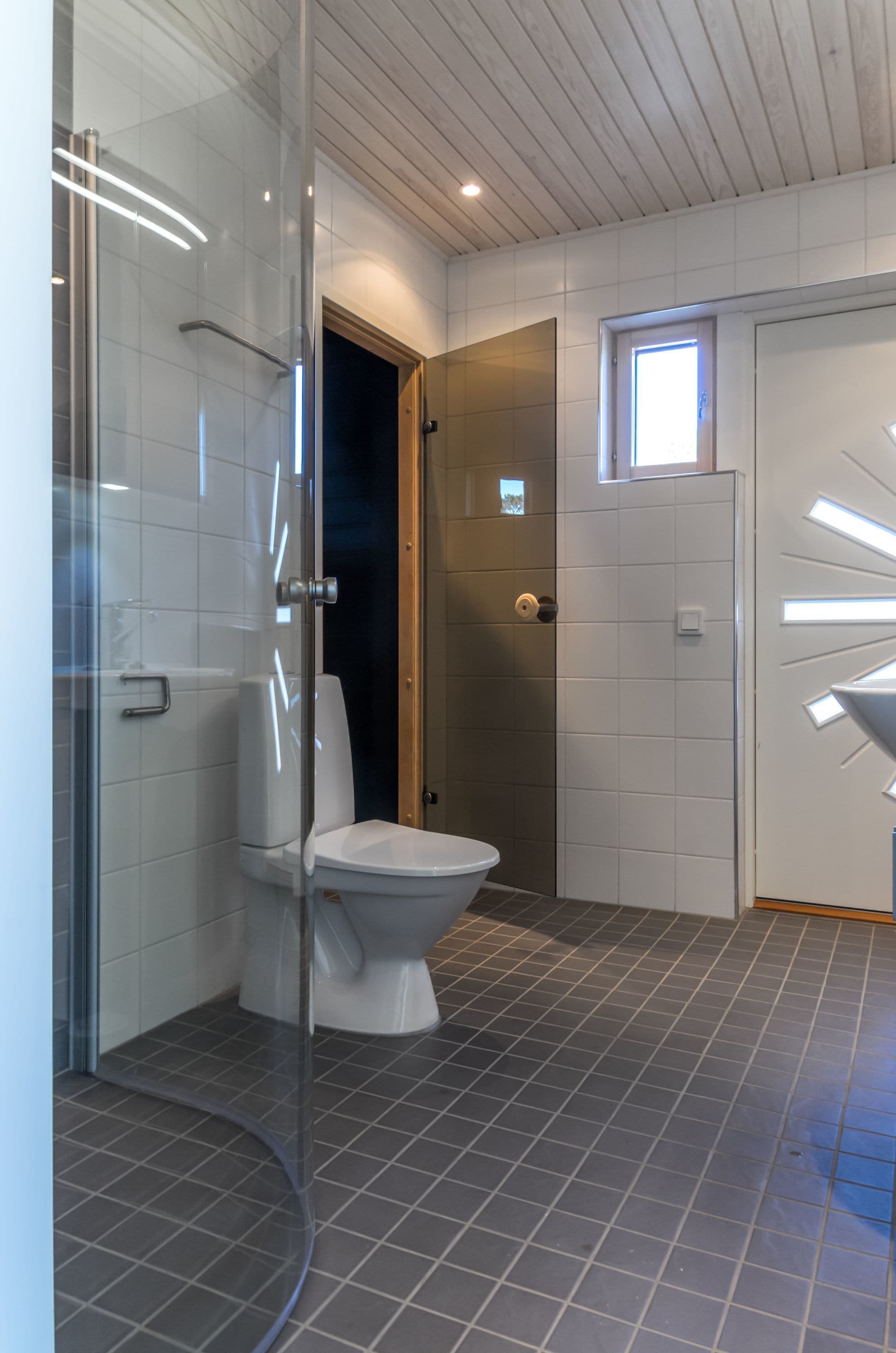A modern bathroom with a glass shower enclosure, a white toilet, and a tiled floor.