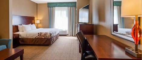 Habitación de hotel con cama, escritorio, silla, lámpara, televisor y ventana con cortinas.