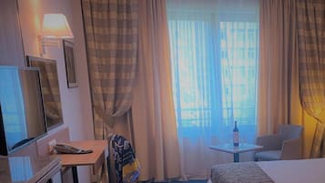 Ett hotellrum med en säng, ett skrivbord, en stol, en tv och ett fönster med gardiner.