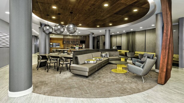A modern interior with a curved ceiling, a sectional sofa, a round coffee table, and a dining area with chairs and a table. - SpringHill Suites by Marriott San Antonio Airport (San Antonio)