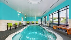 An indoor swimming pool with clear blue water, surrounded by green and black chairs, and a wooden bench. - SpringHill Suites by Marriott San Antonio Airport (San Antonio)