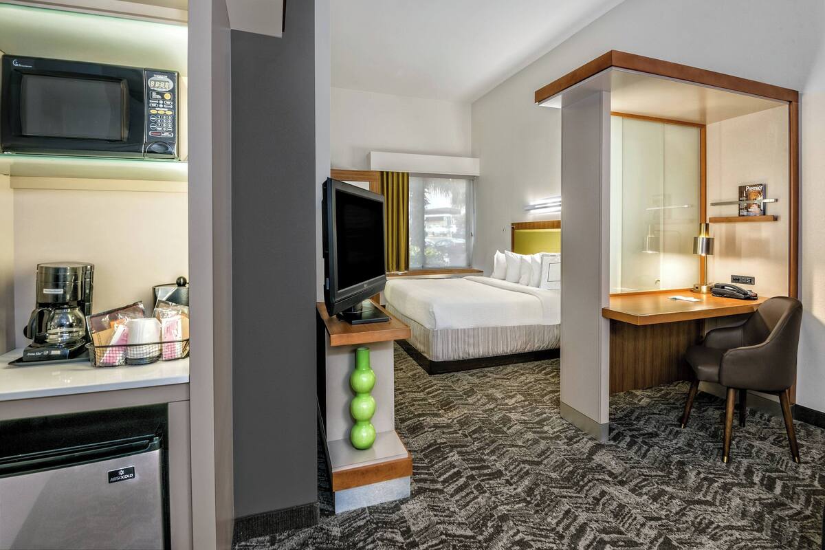 A hotel room with a bed, a desk with a chair, a television, a microwave, and a coffee maker.