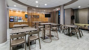 A modern restaurant with round tables and chairs, a counter with a menu, and a TV screen. - SpringHill Suites by Marriott San Antonio Airport (San Antonio)