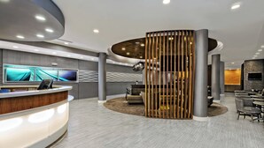 A modern reception area with a curved reception desk, a large flat-screen TV, and a seating area with sofas and a coffee table. - SpringHill Suites by Marriott San Antonio Airport (San Antonio)