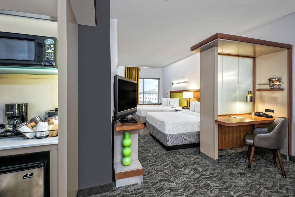 A hotel room with a kitchenette, a TV, a desk, a chair, and a bed.