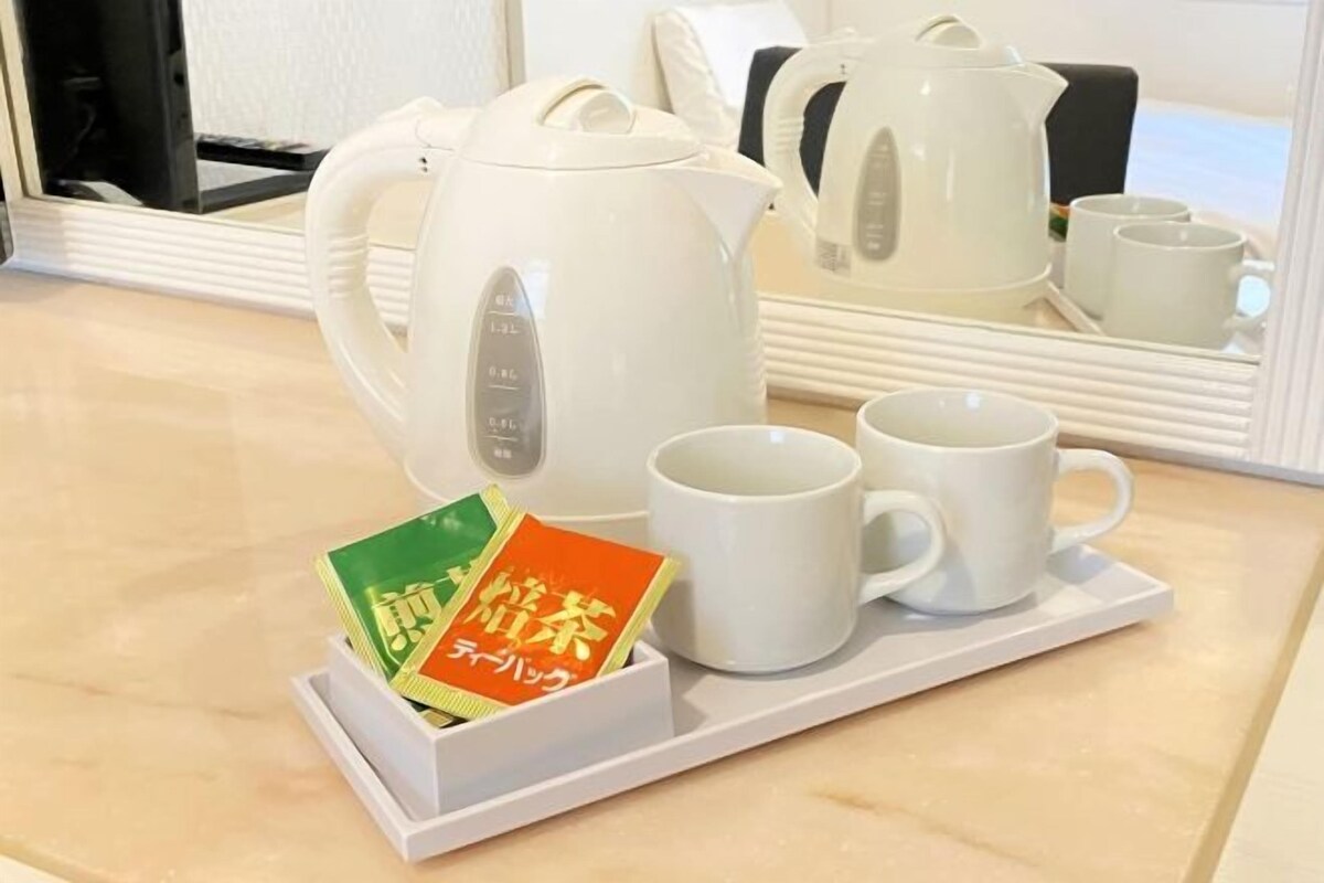 Een witte theeset bestaande uit een waterkoker, twee kopjes en een dienblad met theezakjes.