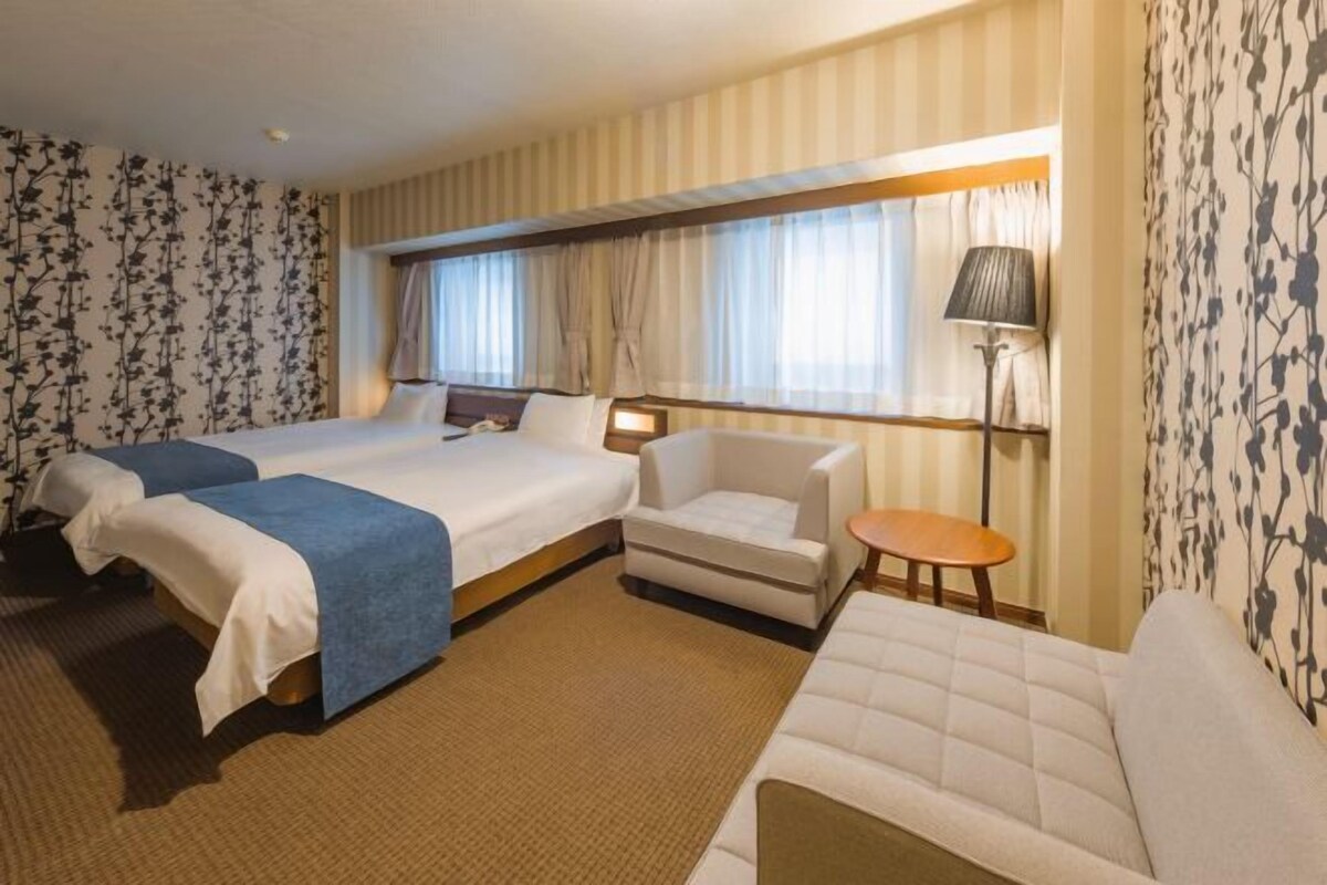 Een hotelkamer met twee bedden, een bank, een kleine tafel en een lamp.