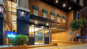 A hotel entrance with a brick facade, glass doors, and a green awning. - New Osaka Hotel (Osaka)