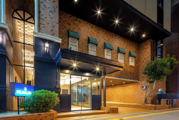 A hotel entrance with a brick facade, glass doors, and a green awning. - New Osaka Hotel (Osaka)