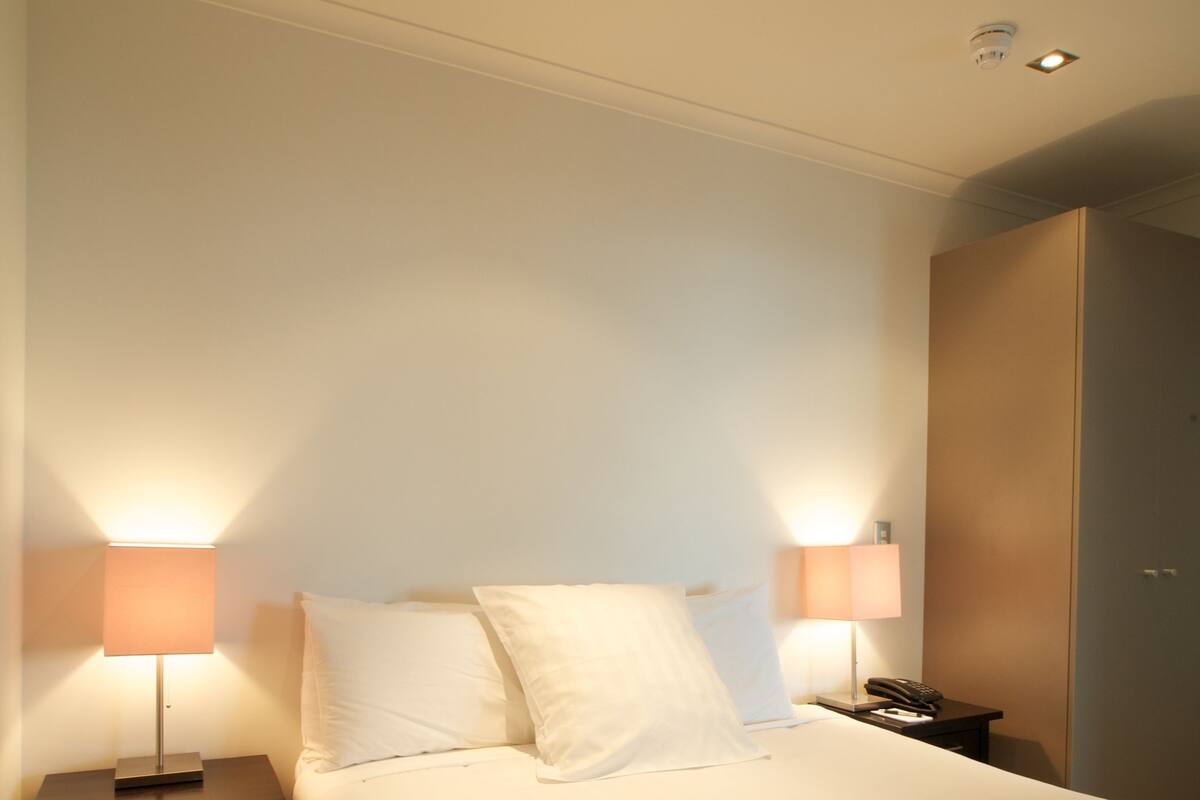A hotel room with a bed, two bedside lamps, a nightstand, and a wardrobe.