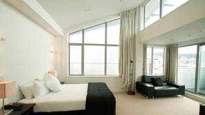 A modern hotel room with a large bed, a sofa, and a view of the city through large windows. - Distinction Wellington Century City Hotel (Wellington)
