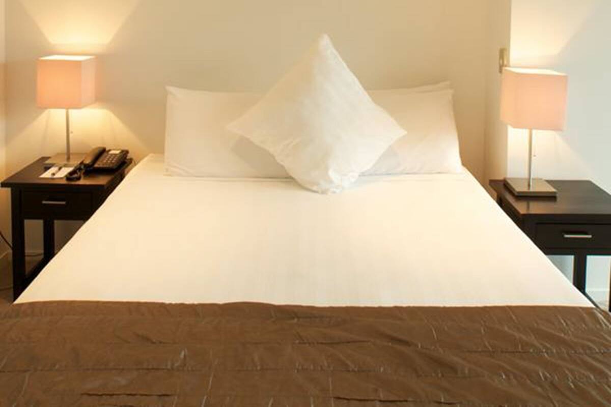 A neatly made bed with white linens and a brown throw blanket, flanked by two bedside tables with lamps and a phone.