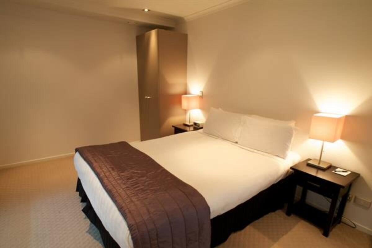 A neatly made bed with a brown blanket, two bedside tables with lamps, and a door in the background.