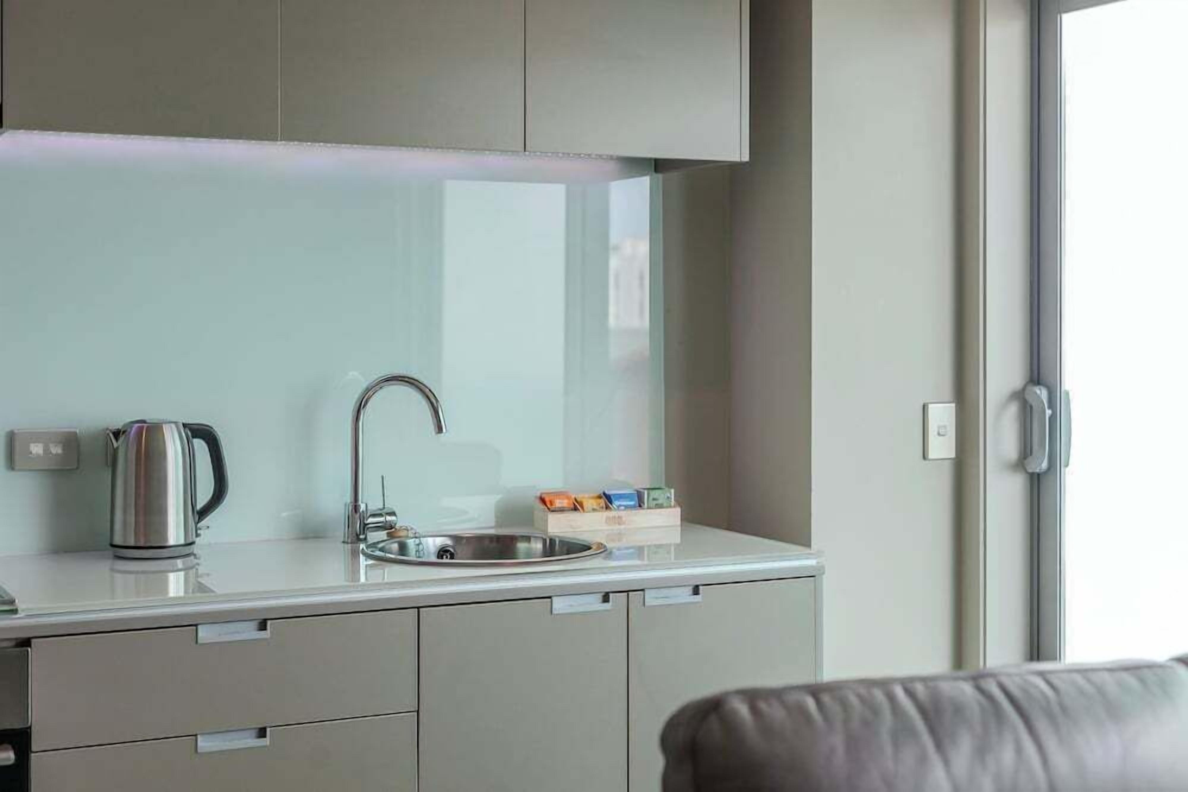 Een moderne kitchenette met een roestvrijstalen waterkoker, een spoelbak en een zeepdispenser.