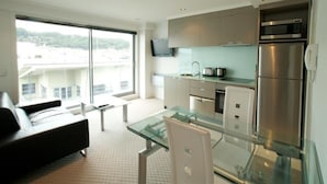 A modern kitchen with a glass dining table, stainless steel appliances, and a view of buildings outside. - Distinction Wellington Century City Hotel (Wellington)