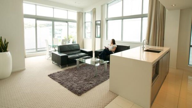 A modern living room with a black leather sofa, a glass coffee table, and a kitchen area with a sink and countertop. - Distinction Wellington Century City Hotel (Wellington)