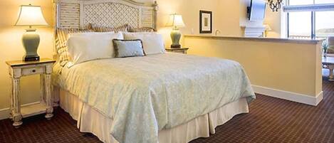A neatly made bed with a headboard, two bedside tables with lamps, a large window, and a chandelier.