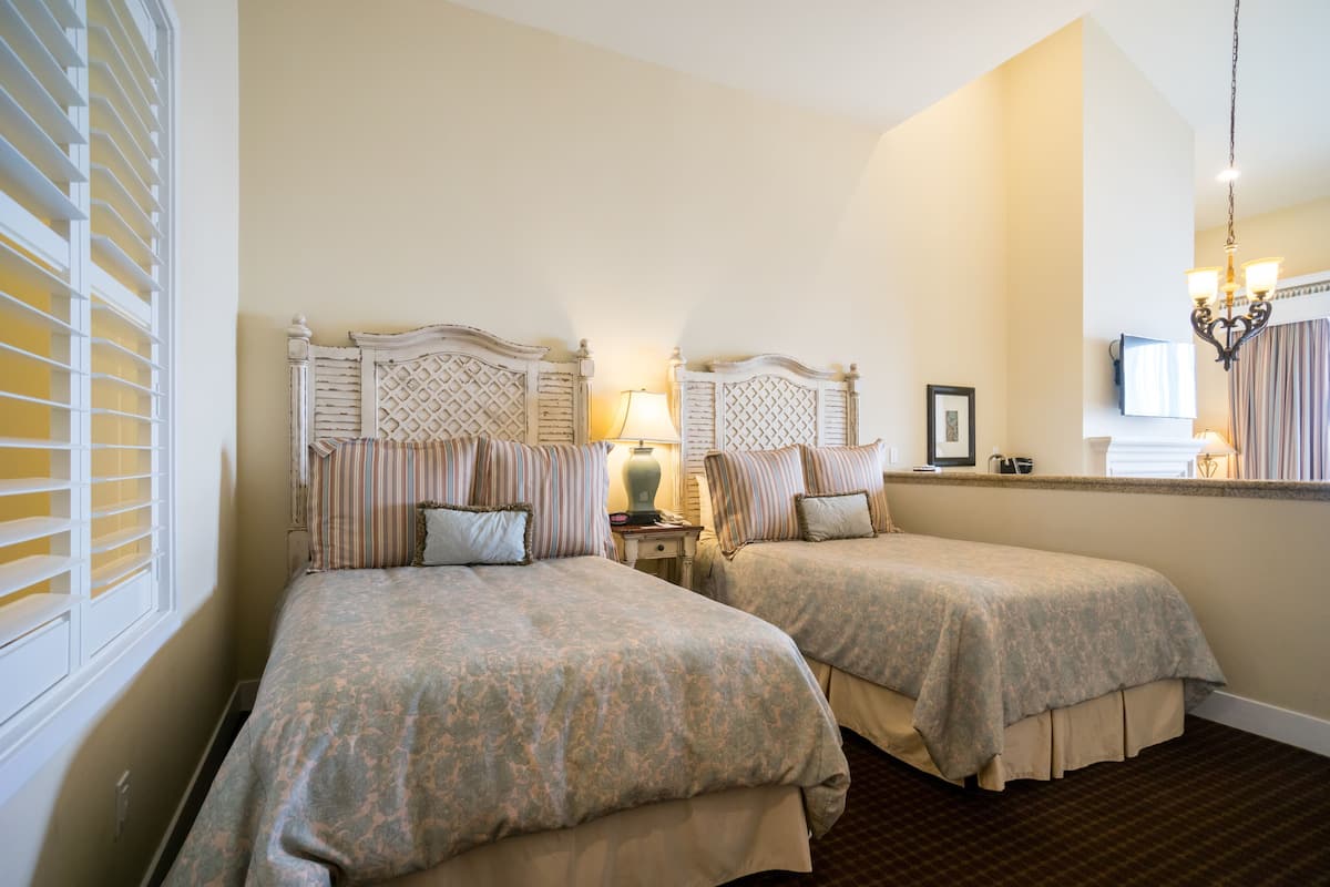 A hotel room with two beds, a nightstand, a lamp, a mirror, and a chandelier.