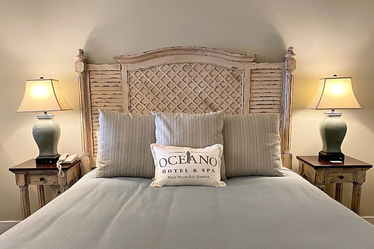 A bed with a headboard, two bedside tables, two lamps, and a pillow with 'OCEANO HOTEL & SPA' text.