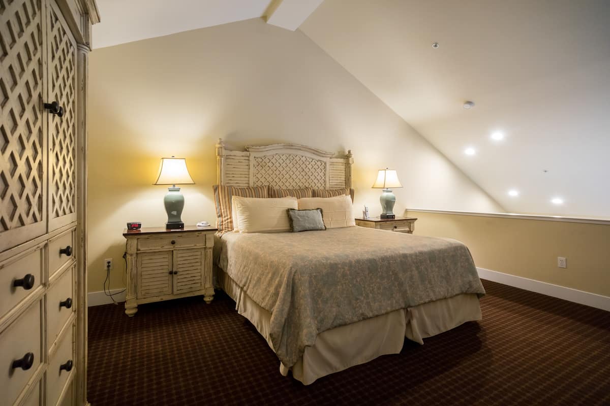 A bedroom with a large bed, two bedside tables with lamps, a dresser with drawers, and a patterned carpet.