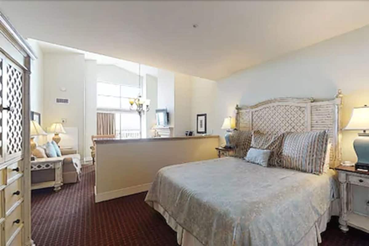 A bedroom with a large bed, two bedside tables with lamps, a dresser, and a window with curtains.